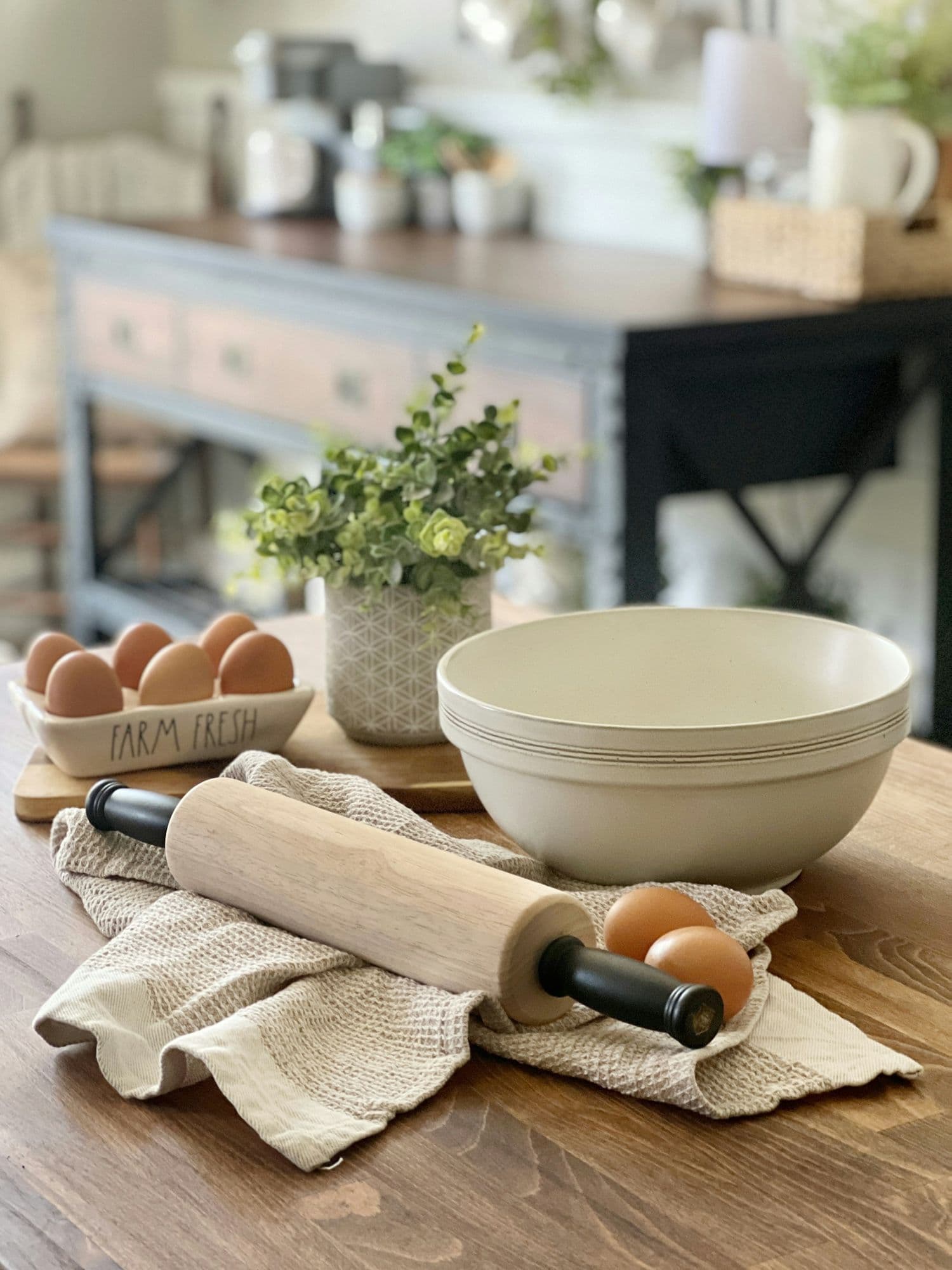 A cream mixing bowl, eggs, a rolling pin, and a potted plant
